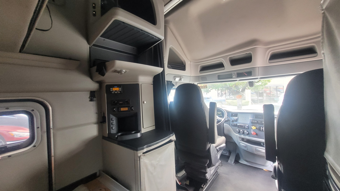 Truck cab interior of a 2021 Peterbilt 579 showing dash and sleeper area with overhead compartments and steering area.