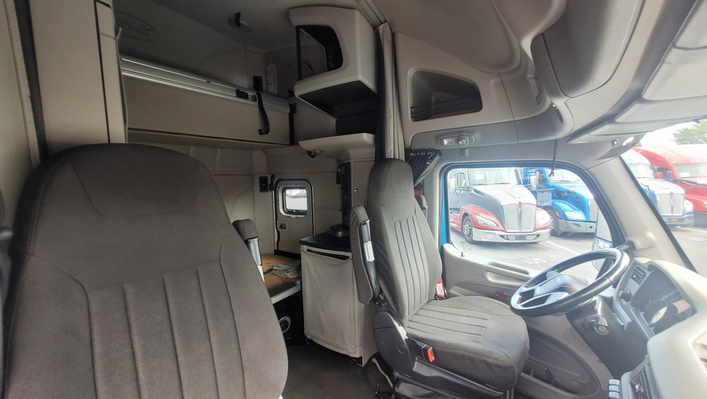 Peterbilt 579 cab interior showing driver seat and dashboard with sleeping area overhead storage.
