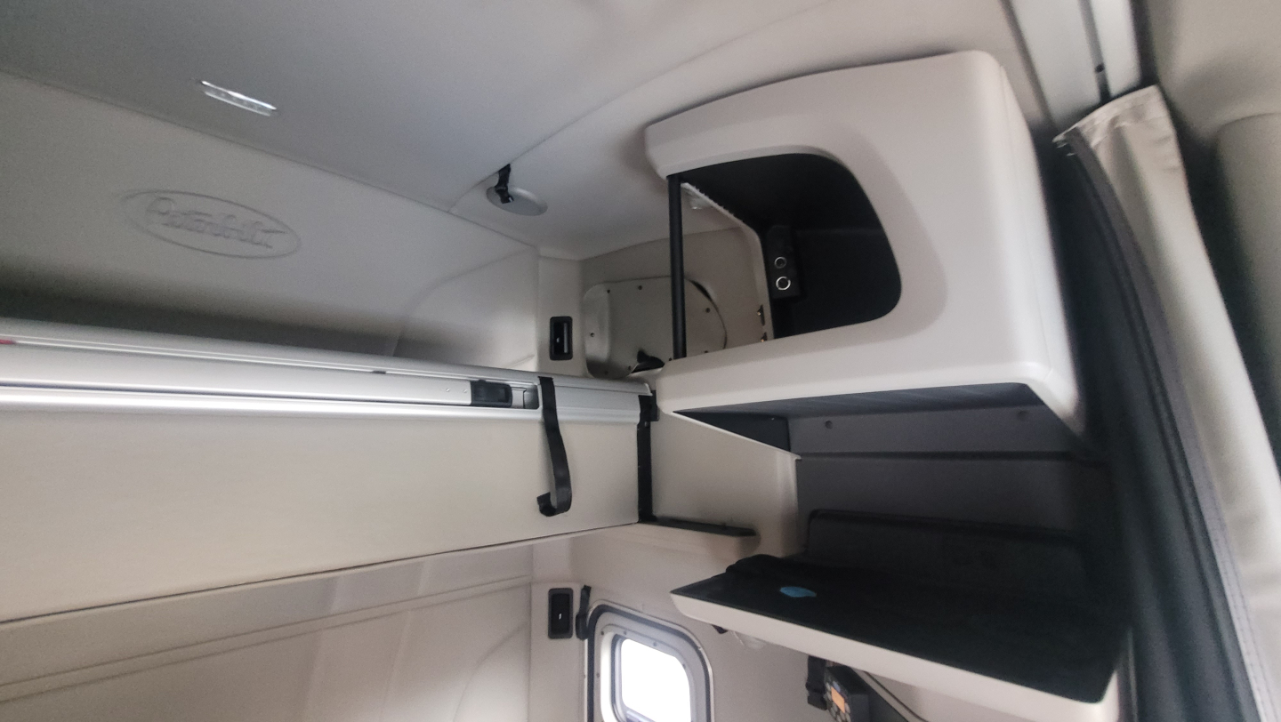 Peterbilt truck cab interior showing upper storage cabinet and sleeping berth area with a small shelf and a closed compartment.
