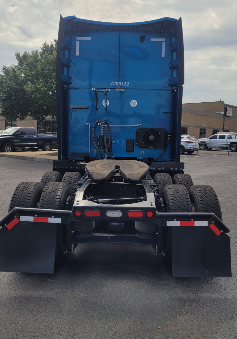 Peterbilt 579 rear view showing blue sleeper cab with fifth wheel and dual rear axles, wheels, mud flaps, and bumper.