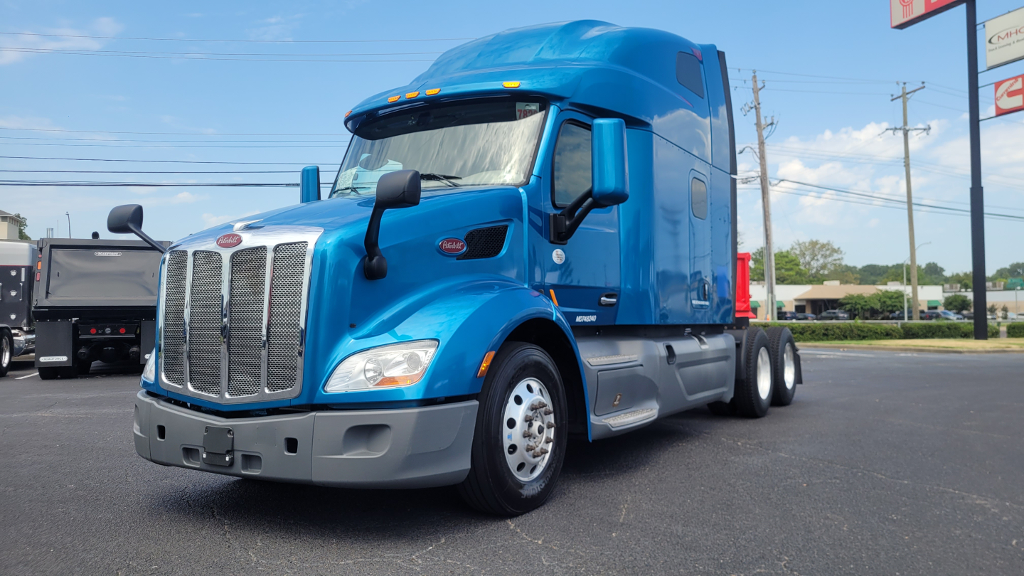 Peterbilt 579 sleeper cab truck in blue, front-left view with grille, headlights, and large side mirrors visible.