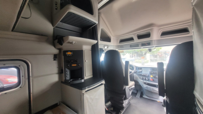 Truck cab interior of a 2021 Peterbilt 579  showing dash and sleeper area with overhead compartments and steering area.