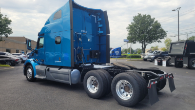 Peterbilt 579 tractor with blue cab, side profile view, sleeper cab, dual rear axles, fifth wheel, exposed fuel tanks, and chrome wheels.