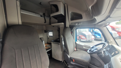 Peterbilt 579 cab interior showing driver seat and dashboard with sleeping area overhead storage.