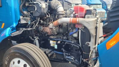 Peterbilt 579 engine bay showing coolant reservoir, air intake hose, turbocharger, and frontal engine components.