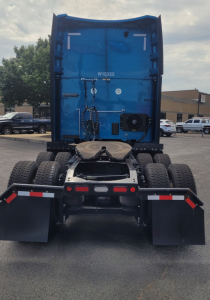 Peterbilt 579 rear view showing blue sleeper cab with fifth wheel and dual rear axles, wheels, mud flaps, and bumper.