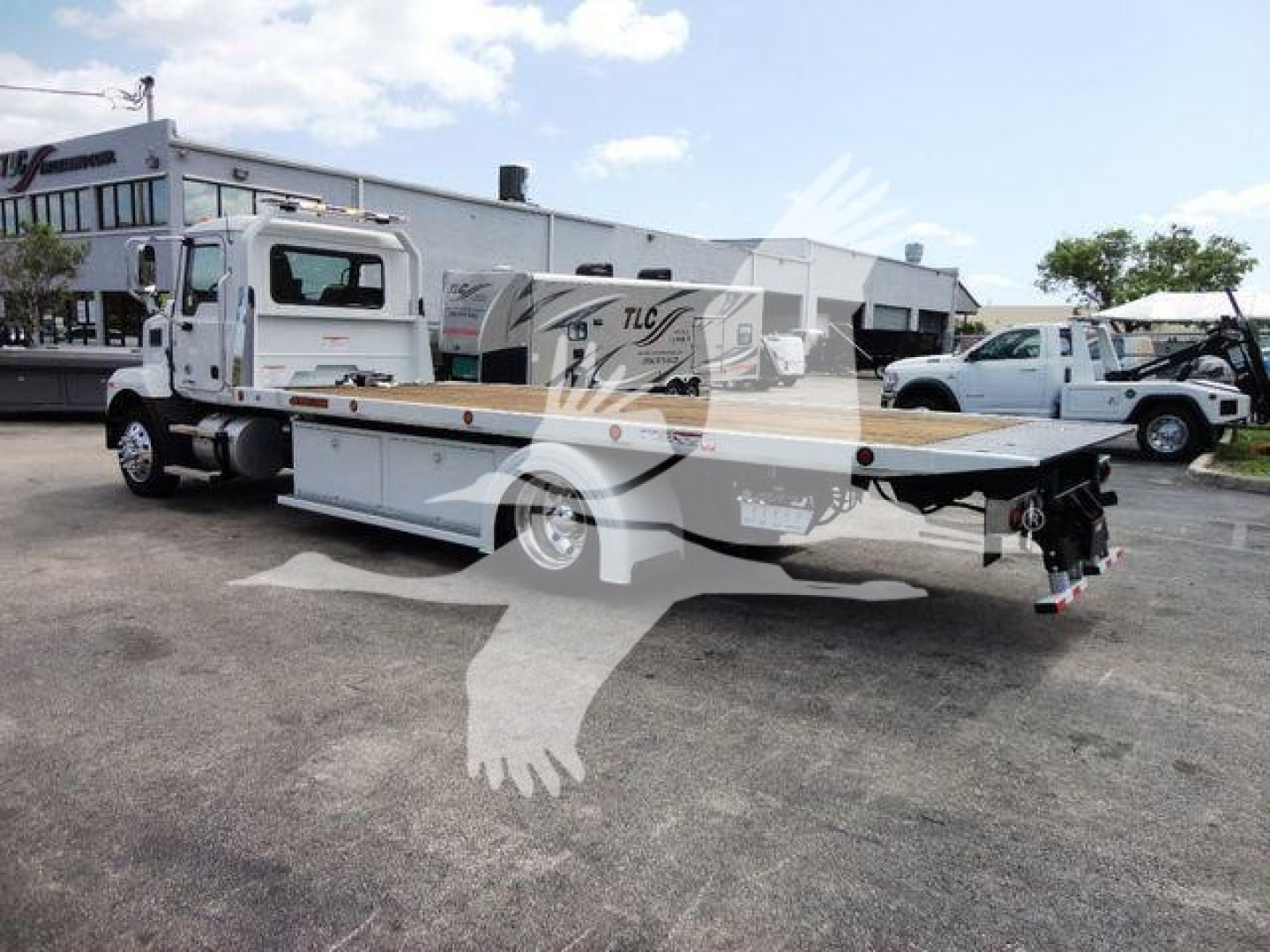 Flatbed tow truck in a dealership lot showing Mack MD6 cab and flatbed with equipment tags.