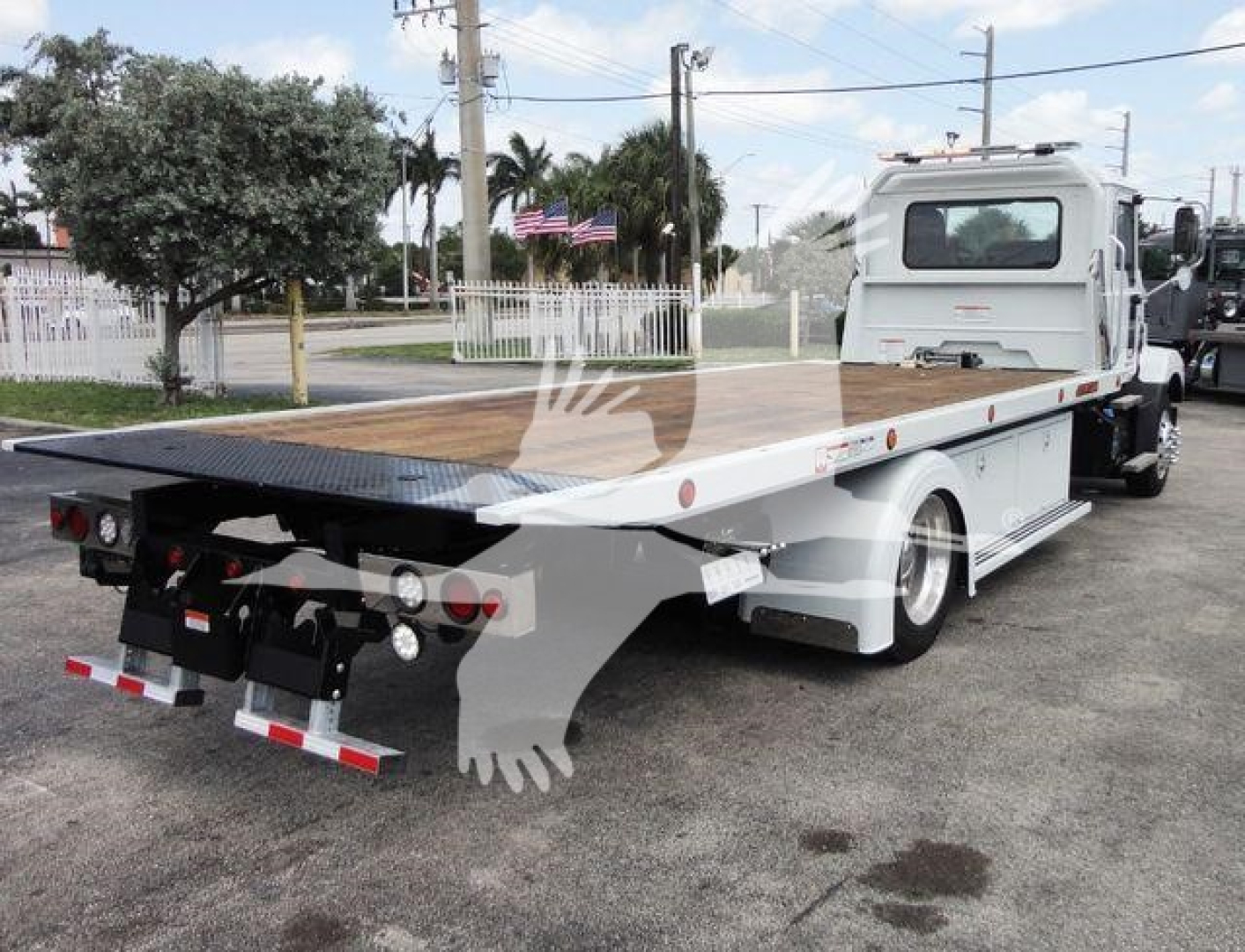 Flatbed tow truck from rear-right angle showing long aluminum deck and rear hitch, Mack MD6 rollback with white cab and black flatbed