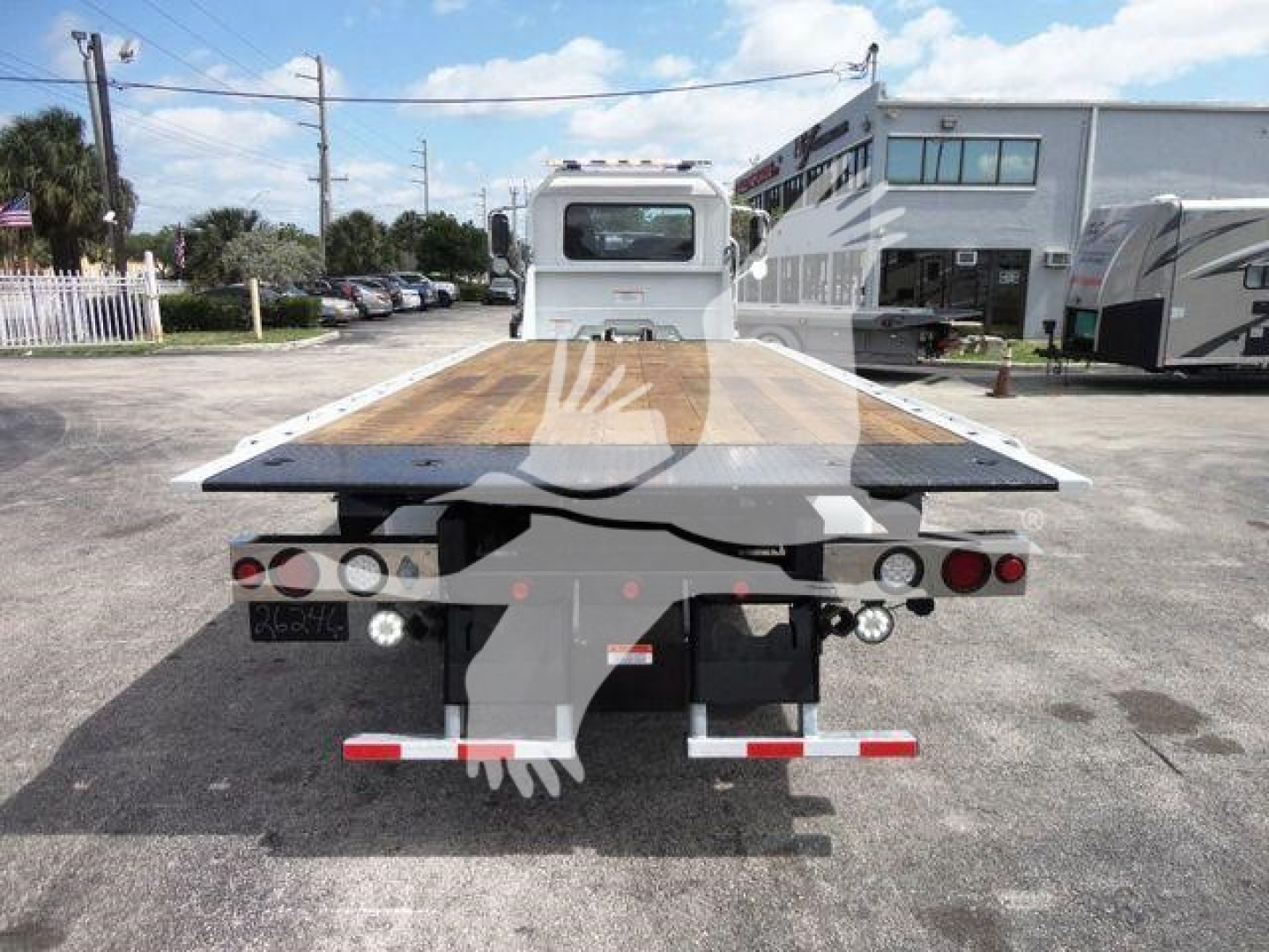 Mack MD6 rollback flatbed truck rear view showing wooden bed surface, taillights, and hitch components in a dealership lot.