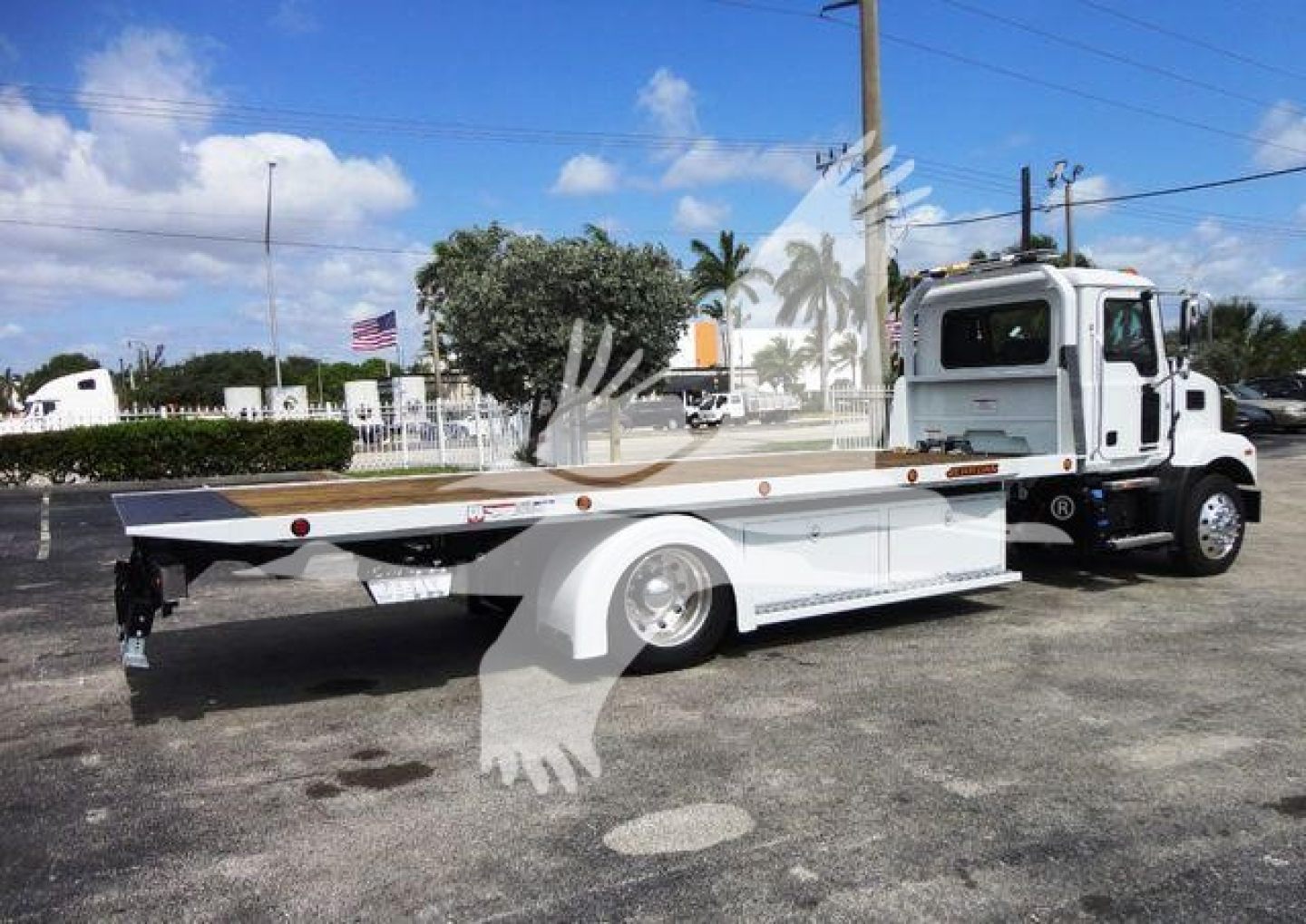 Flatbed tow truck on dealership lot with Mack MD6 cab and rollback bed, side view showing flat platform and wheel fenders.
