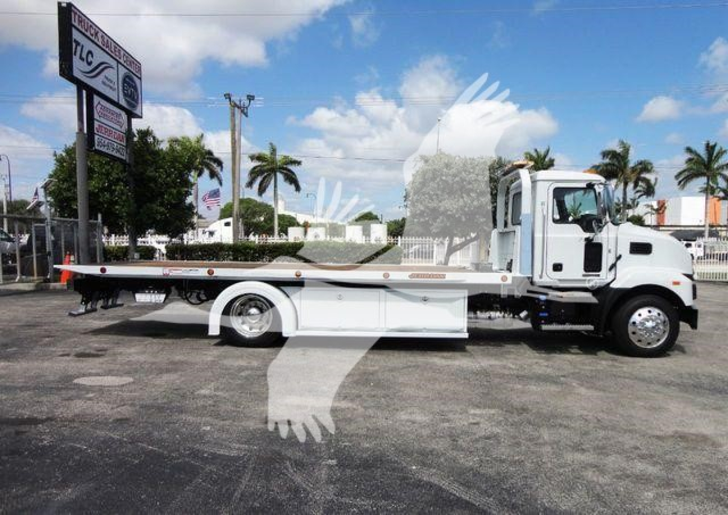 MD6 Mack rollback truck side view showing flatbed and towing equipment with white cab on a dealership lot.