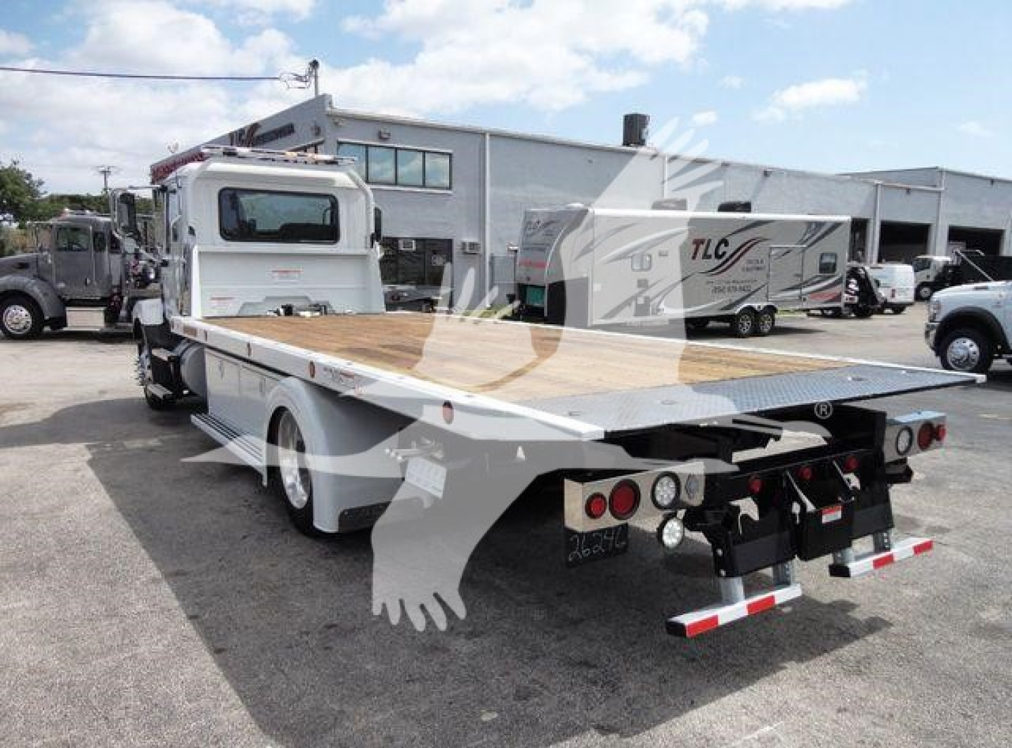 2026 Mack MD6 rollback truck rear view showing flatbed with wooden deck and hydraulic winch, rear lights, and towing equipment.