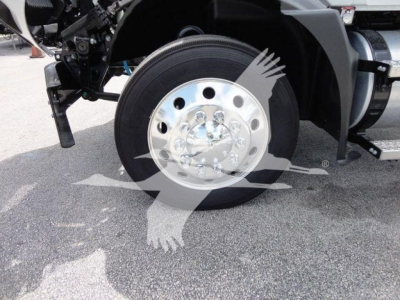 Wheel and front axle area of a 2026 Mack MD6 rollback truck showing polished aluminum wheel with black tire and surrounding chassis components.