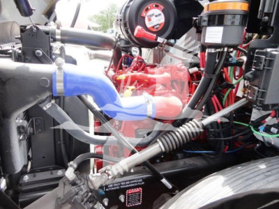MD6 engine bay showing blue coolant hose, red components, wiring loom, and various hydraulic lines in a Mack truck cab interior.