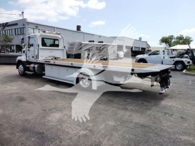 Flatbed tow truck in a dealership lot showing Mack MD6 cab and flatbed with equipment tags.
