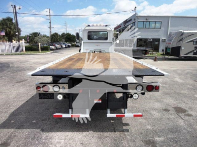 Mack MD6 rollback flatbed truck rear view showing wooden bed surface, taillights, and hitch components in a dealership lot.