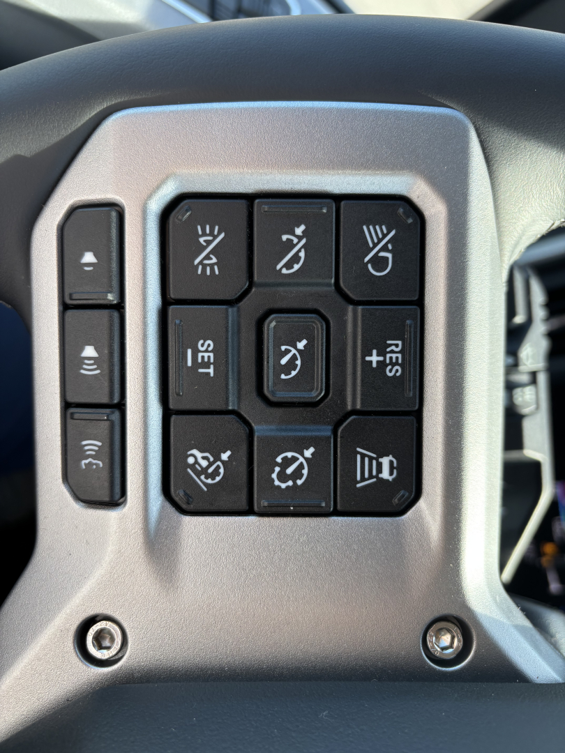 Steering wheel control panel with multiple buttons, including cruise control and lighting icons, in a Mack AN64T truck interior, close-up view.