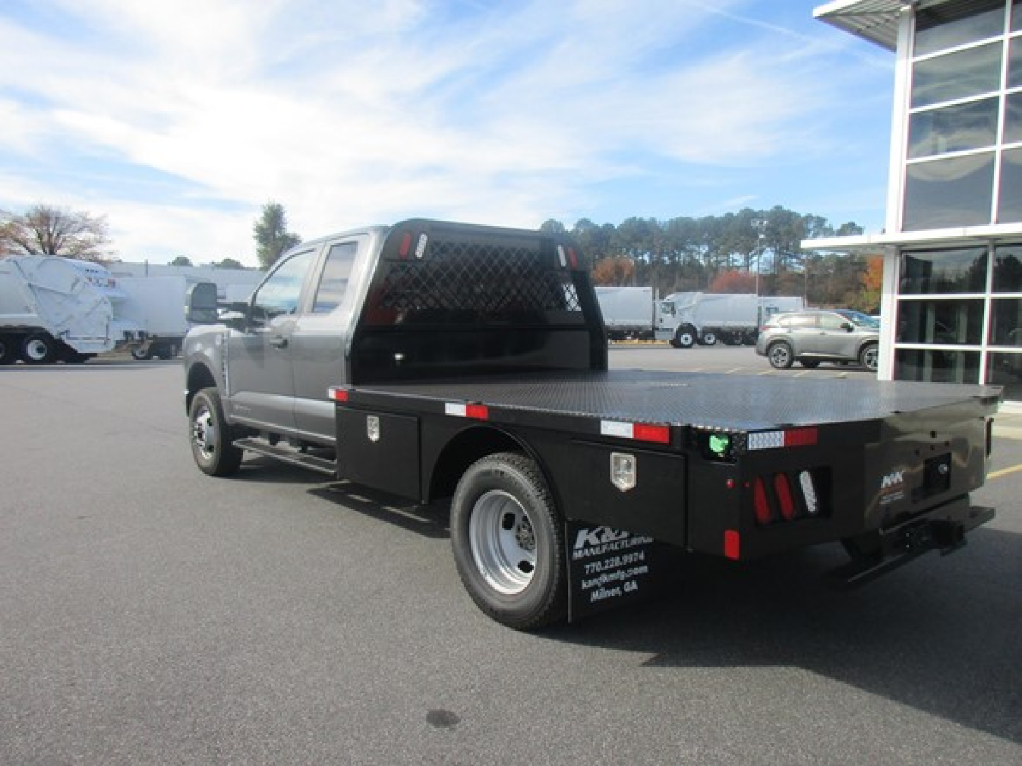 Flatbed tow truck rear-left side showing sturdy black flatbed with storage boxes, rear lights, and metal diamond plate, NY-based dealer markings on the cab/back.