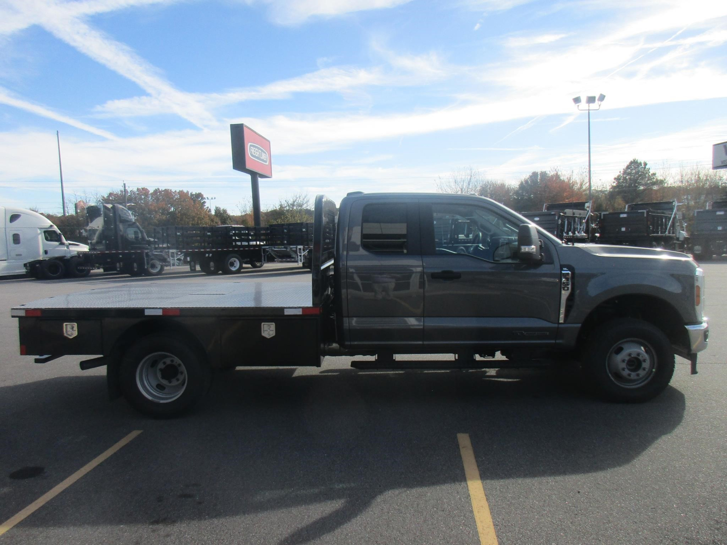 2026 Ford F350 Super Duty crew cab flatbed truck in a dealership lot, side view showing a flatbed with toolboxes and dual rear wheels.