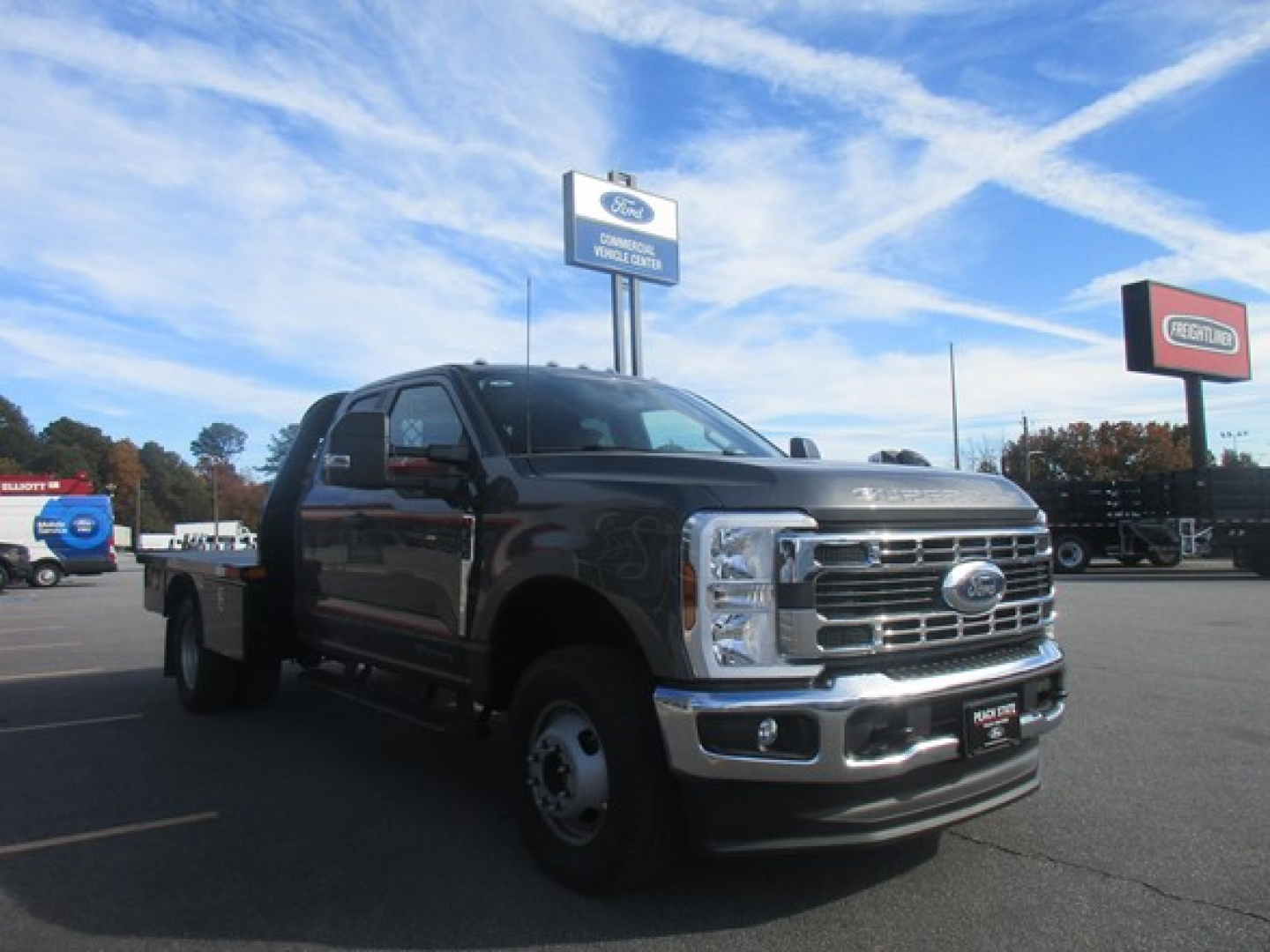 Ford F-350 flatbed truck in dealership lot with chrome grille and dual rear wheels, front-left view.