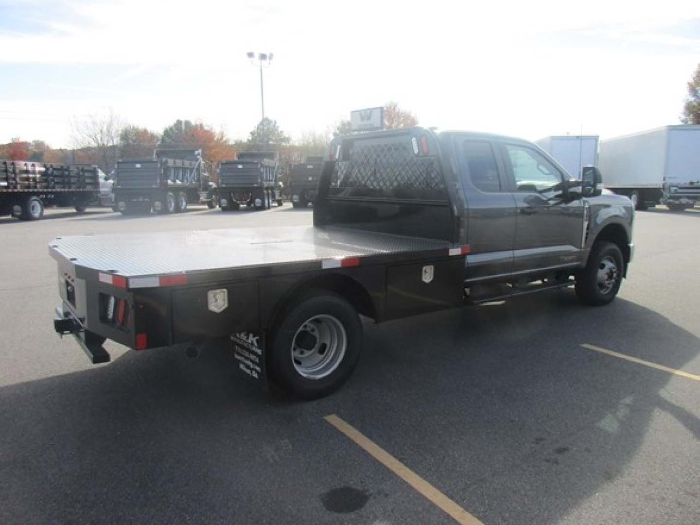 Flatbed truck with dual rear wheels showing a metal flatbed and cab in a dealership lot.