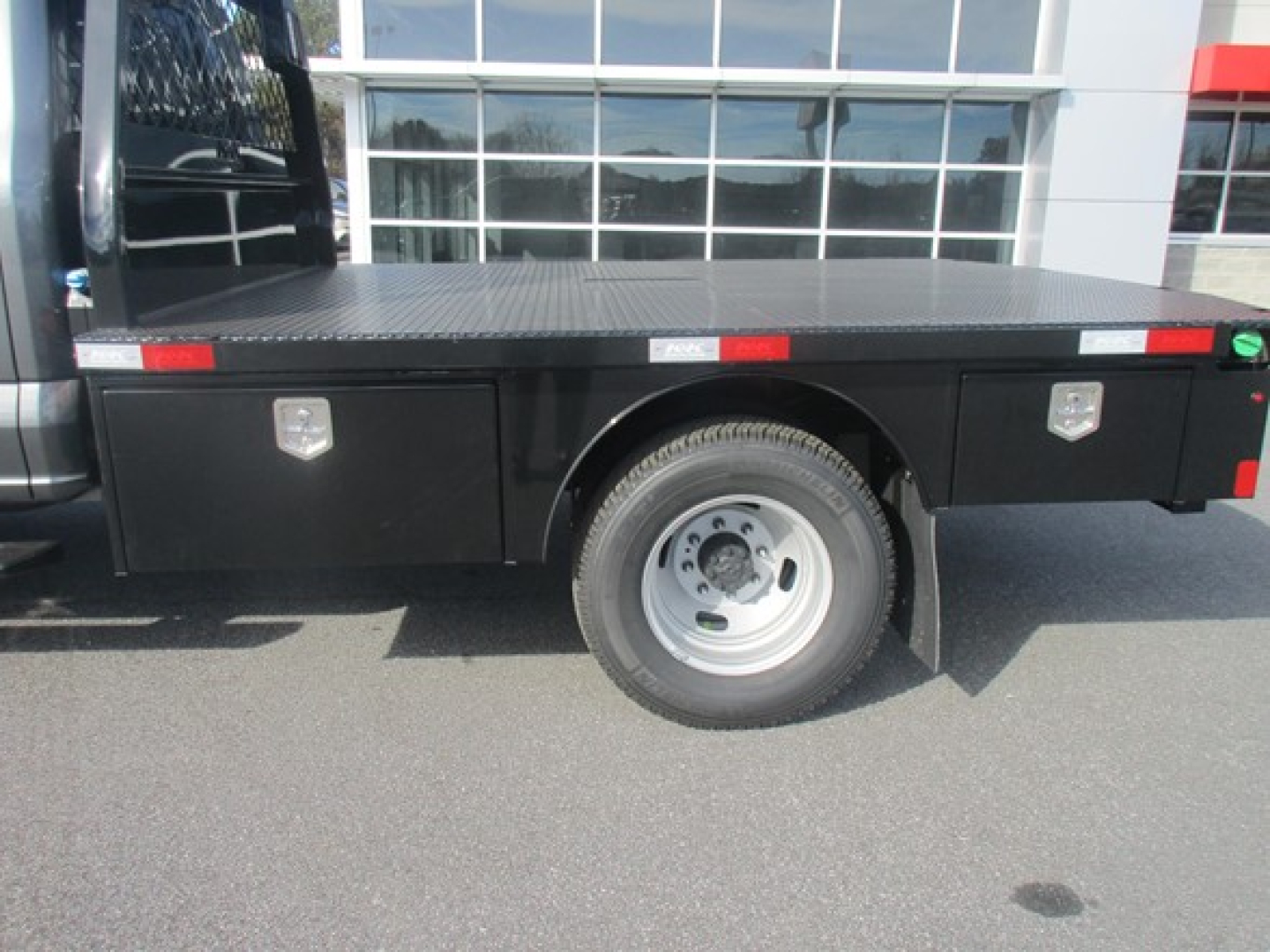 Flatbed truck bed with single rear wheel and side compartments on Ford F350 chassis, metal diamond plate deck visible.