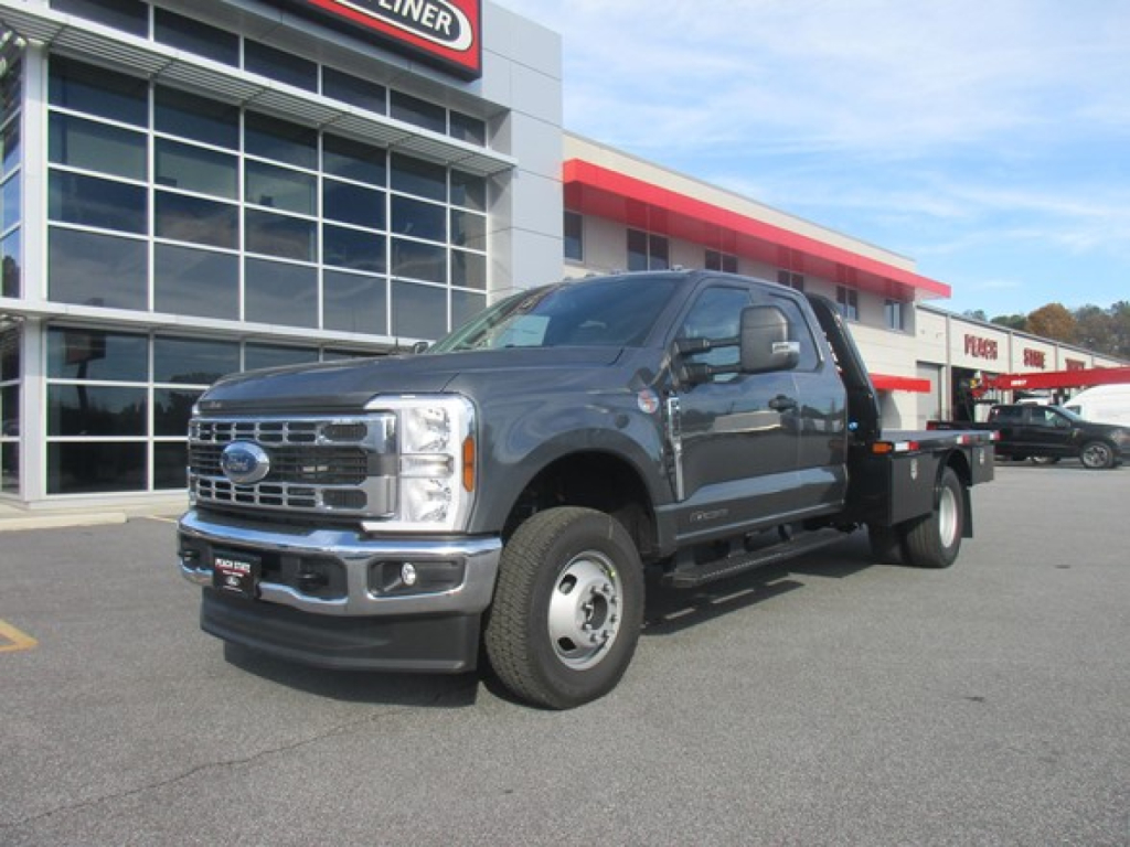 2026 Ford F-350 SD flatbed truck in dealership lot showing front grille with Ford emblem and large cab; building with glass windows in background.