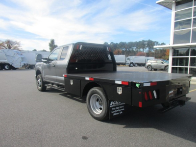 Flatbed tow truck rear-left side showing sturdy black flatbed with storage boxes, rear lights, and metal diamond plate, NY-based dealer markings on the cab/back.