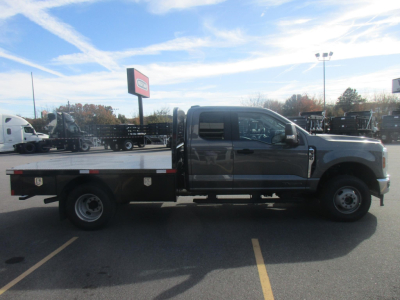 2026 Ford F350 Super Duty crew cab flatbed truck in a dealership lot, side view showing a flatbed with toolboxes and dual rear wheels.