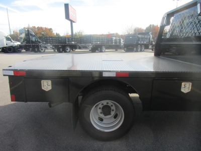 Flatbed truck side view of a new Ford F-350, wheel and dual toolbox area visible, with diamond plate flatbed and reflective markers.