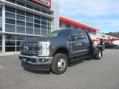 2026 Ford F-350 SD flatbed truck in dealership lot showing front grille with Ford emblem and large cab; building with glass windows in background.