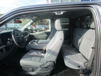 Ford F-350 Super Duty interior showing front bucket seat and rear bench seat with light gray upholstery; front steering wheel and dashboard visible; open driver-side door.