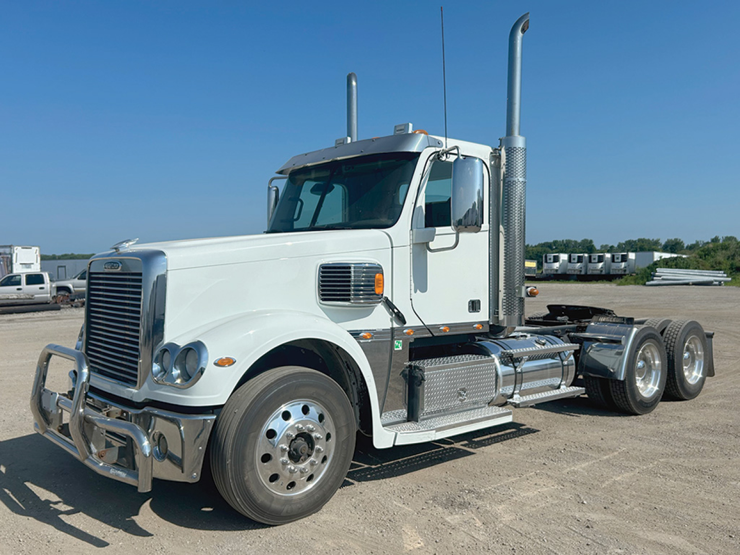 Freightliner Coronado tractor unit in light color showing front grille, dual vertical exhaust stacks, and side fuel tanks.