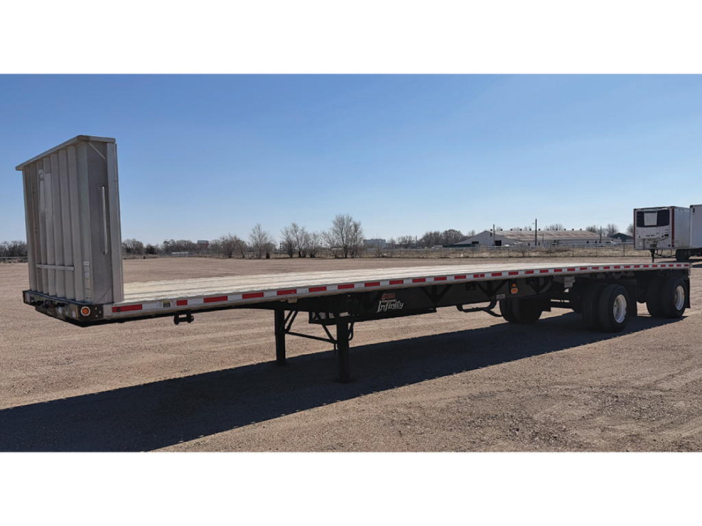 Flatbed trailer showing Fontaine Infinity branding with long deck, rear dual wheels, and a raised gooseneck area; empty cargo area in an open lot.