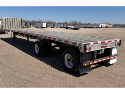 Flatbed trailer showing dual rear axles and aluminum deck with reflective tape along sides.