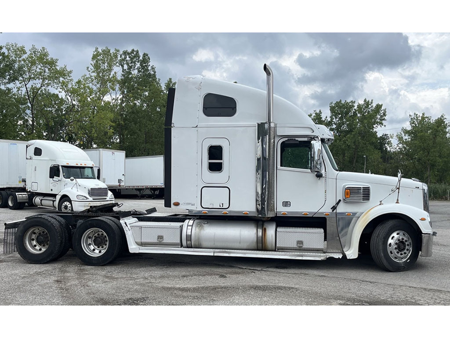 Truck side view showing a white 2015 Freightliner Coronado tractor with a sleeper cab, chrome fuel tanks, and dual rear axles.