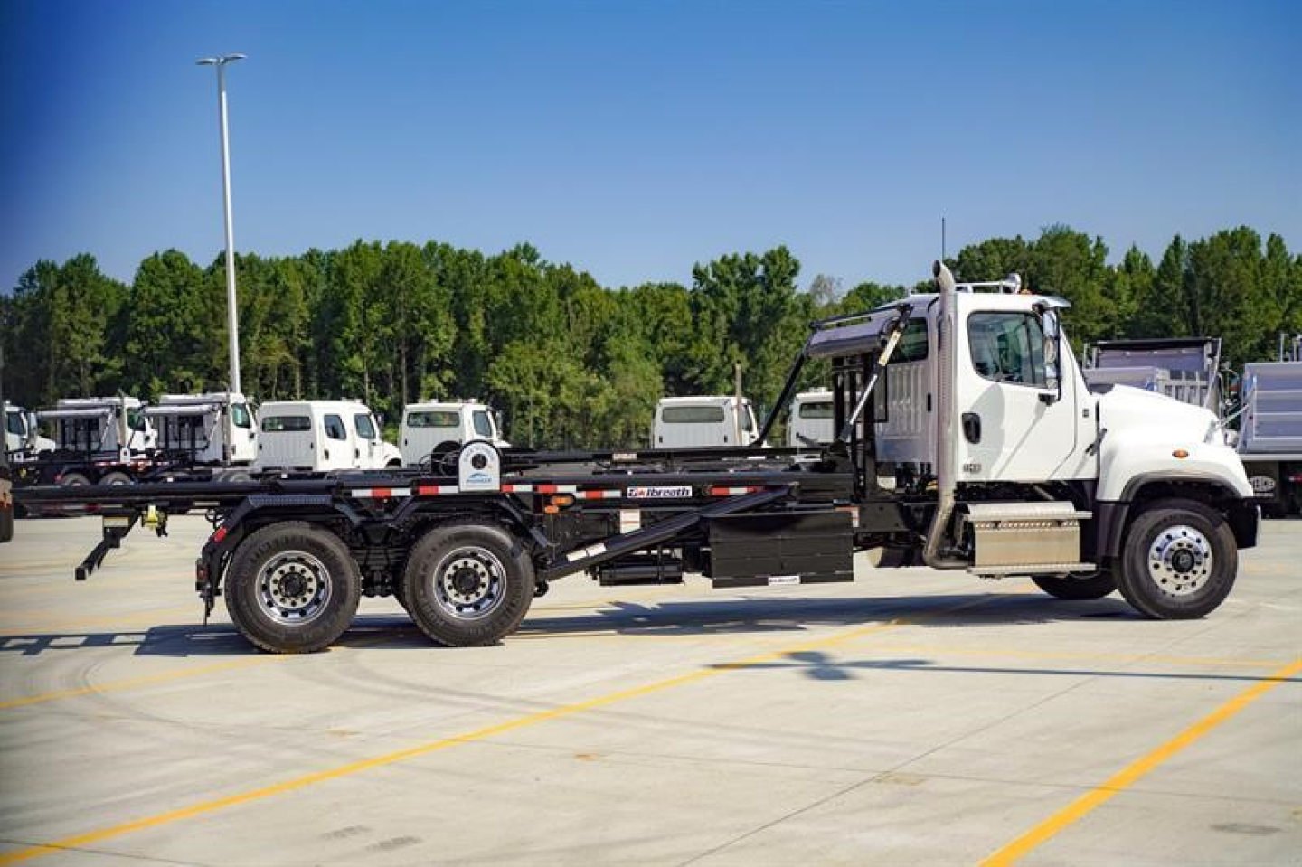 Flatbed tow truck in a parking lot showing Freightliner 114SD chassis with a roll-off bed and white cab.