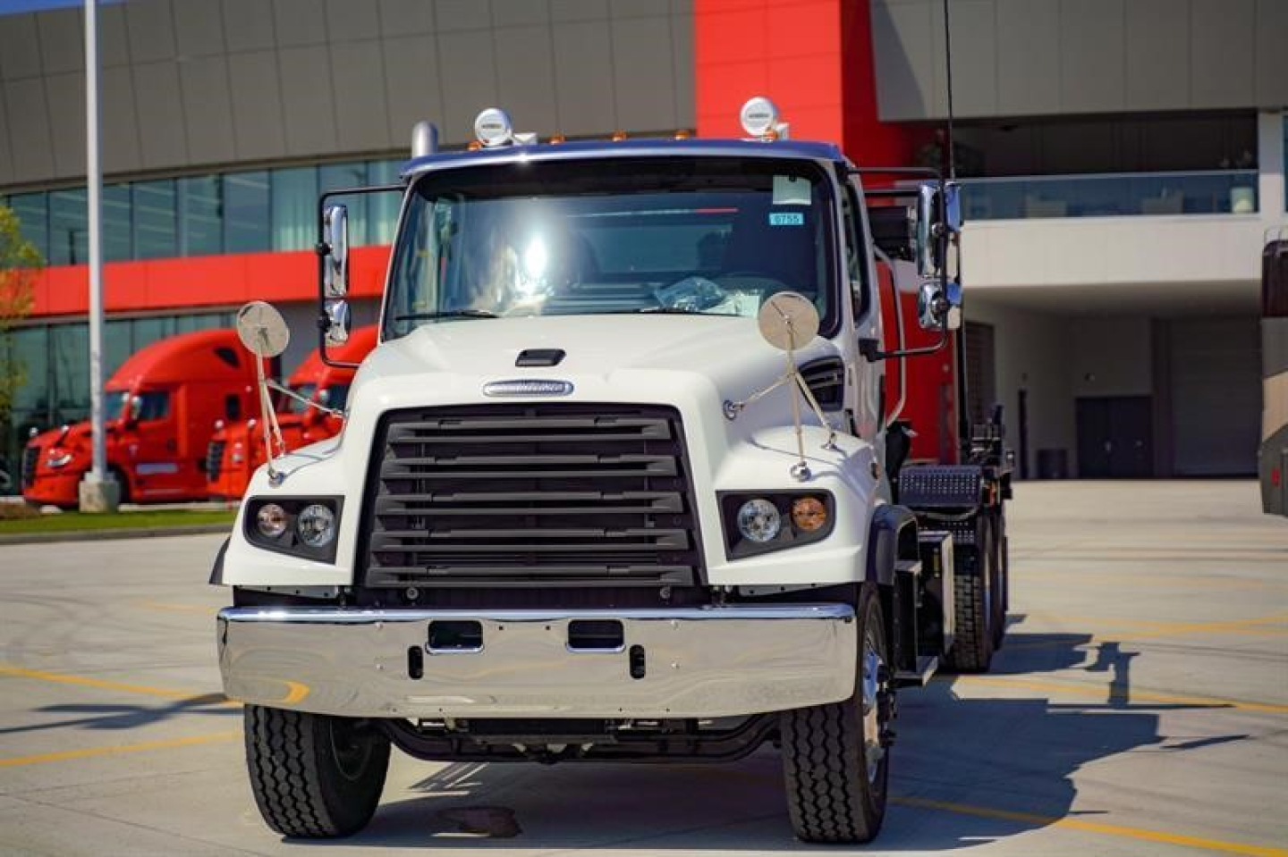 Truck front view of a white Freightliner 114SD roll-off truck with black grille and chrome bumper.