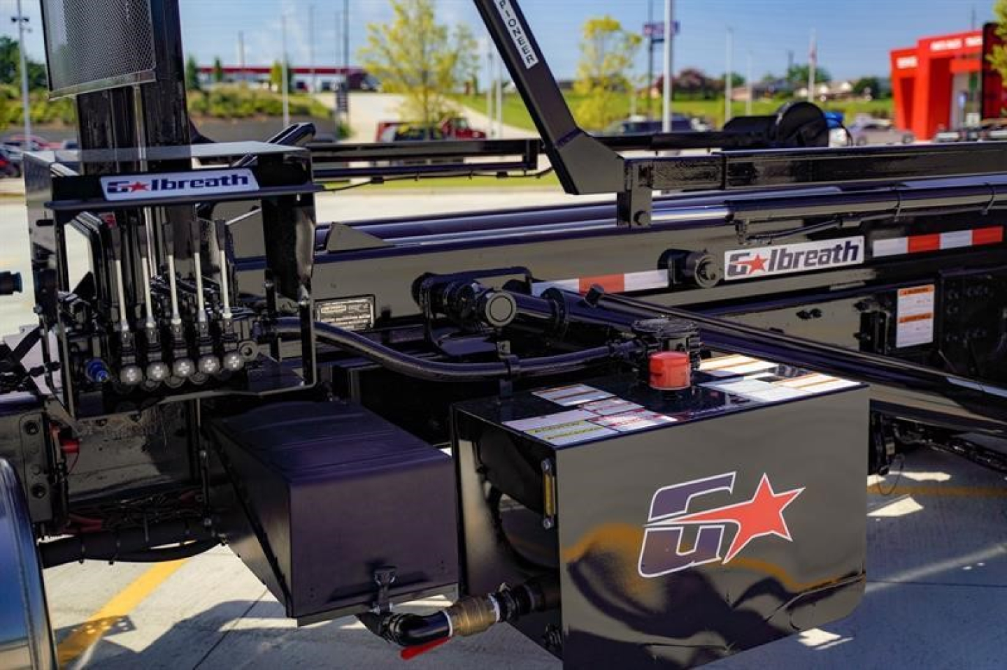 Freightliner 114SD rolloff truck bed showing hydraulic hoses, Brough machinery, and a black toolbox with a star logo; labels read ‘breath’ and hydraulic controls on left; stock and VIN info not visible.