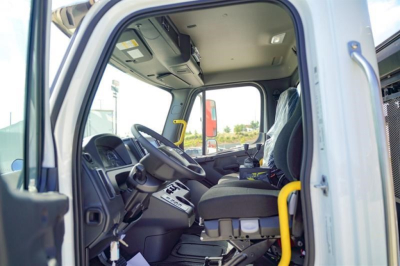 Cab interior of a 2027 Freightliner 114SD roll-off truck showing steering wheel, driver seat, dashboard, and entry door frame.