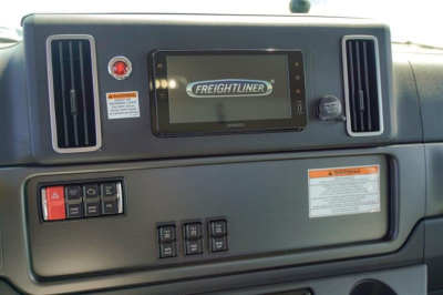 Freightliner 114SD dashboard showing Kenworth-style screen with Freightliner logo, two vertical air vents, control panel, warning labels, and knob.