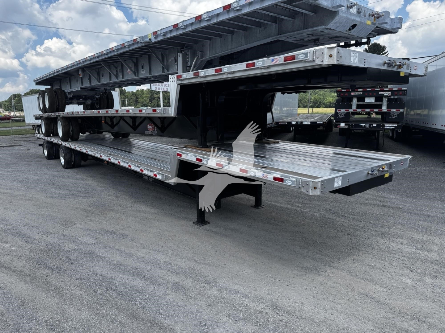 Flatbed trailer with extendable drop deck system and multiple axles parked on lot; aluminum or steel frame; visible hazard markers and reflective tape.