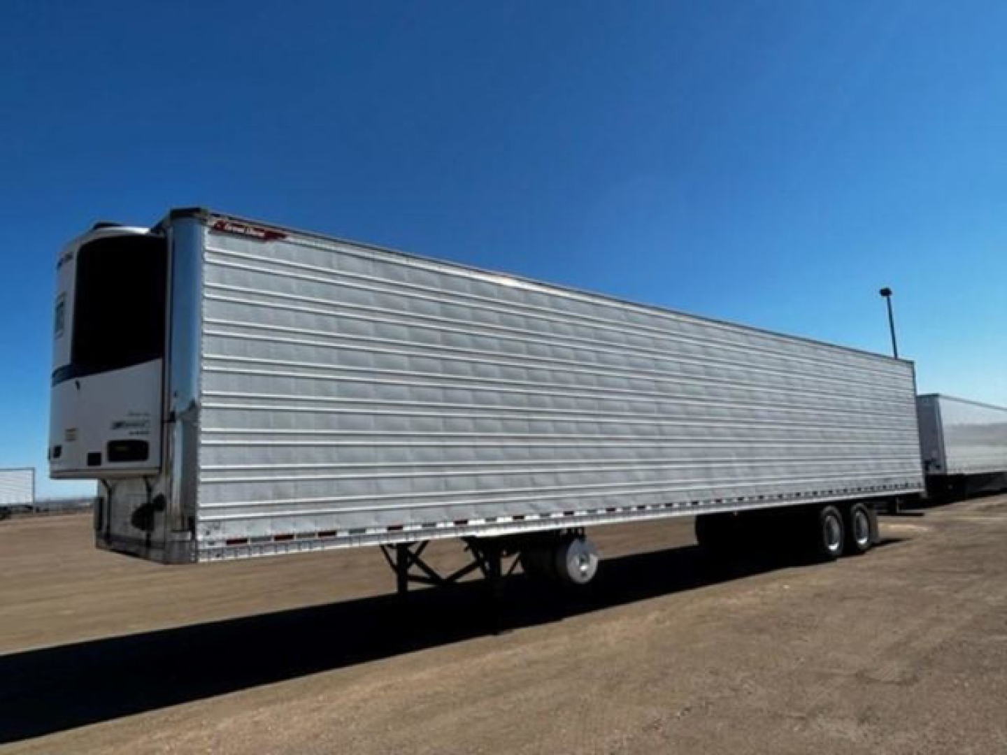 Great Dane refrigerated trailer viewed from side/rear, silver corrugated metal walls, refrigeration unit at front, tandem axles, empty road surface.