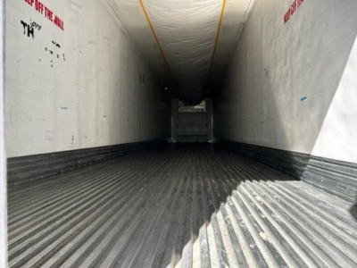 Trailer interior showing long refrigerated box with ribbed metal floor and white sidewalls; door ramp at far end; yellow ceiling support line.