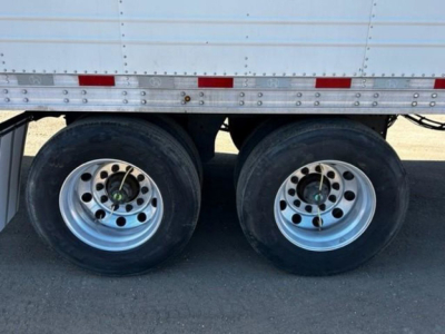 Two rear wheels of a refrigerated trailer with silver rims and black tires; lower side of aluminum trailer with rivets and red reflectors.