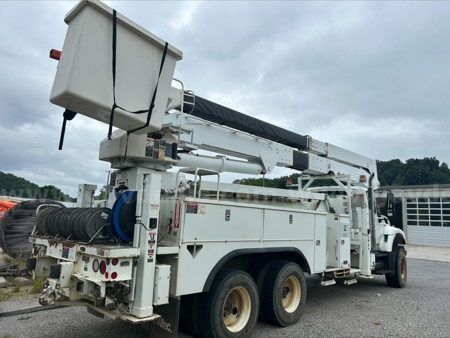 Truck-mounted utility body with bucket lift and hose reels showing multiple compartments and controls. rear view shows tires and hydraulic components.