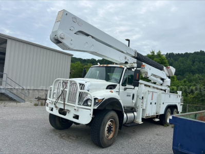 Wide angle view of a 2010 International 7500 bucket truck with boom arm elevated, white utility body, large front bumper guard, and dual rear wheels.