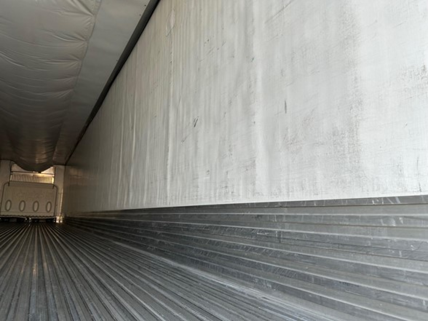 Trailer interior showing metal ribbed floor and white walls, long corridor toward rear with light at far end.