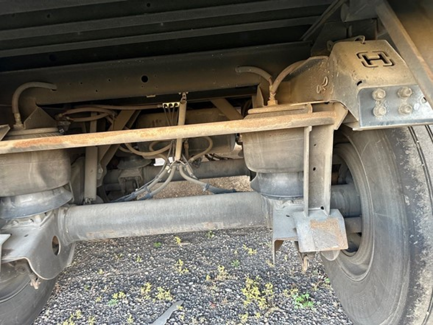 Trailer rear undercarriage showing air ride system components and suspension, with metal frame, axles, hoses, and tire visible.