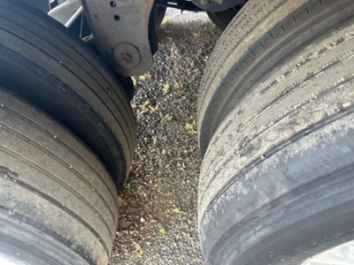 Trailer tires and suspension undercarriage visible; two large tires with tread and road grime; portion of frame and air ride components visible.